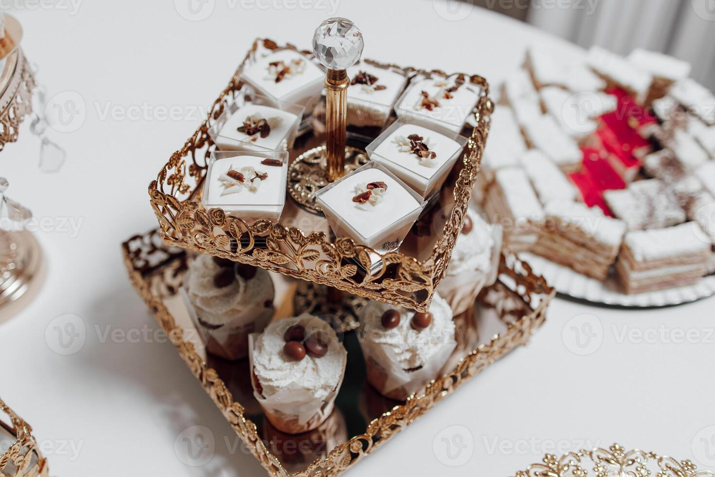 A table with a gold tray holding a variety of desserts, including cupcakes and cakes. The desserts are arranged in a way that makes them look appealing and inviting. The table setting creates a warm photo