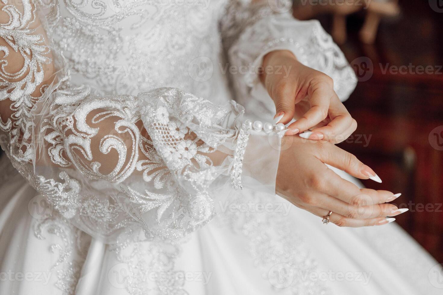 A woman is getting ready for a wedding and is adjusting the lace on her dress. The dress is white and has a lace collar. The woman is wearing a ring on her finger photo