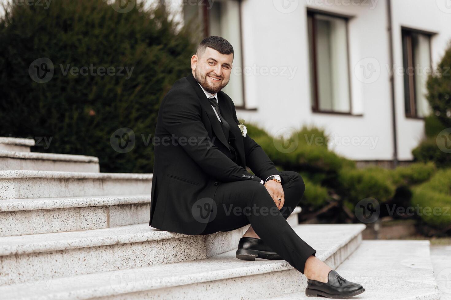 A man in a suit is sitting on a set of stairs. He is smiling and he is enjoying himself photo