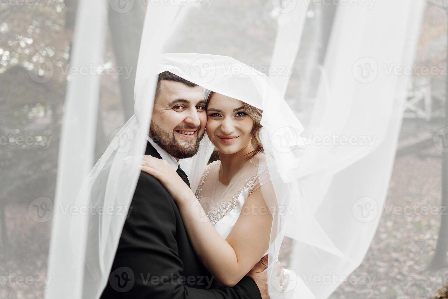 A bride and groom are posing for a picture under a white veil photo