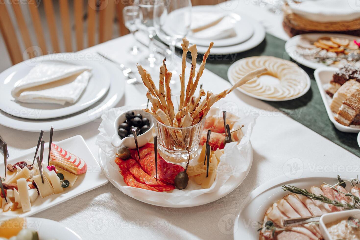 A table with a variety of food, including a plate of breadsticks and a bowl of olives photo
