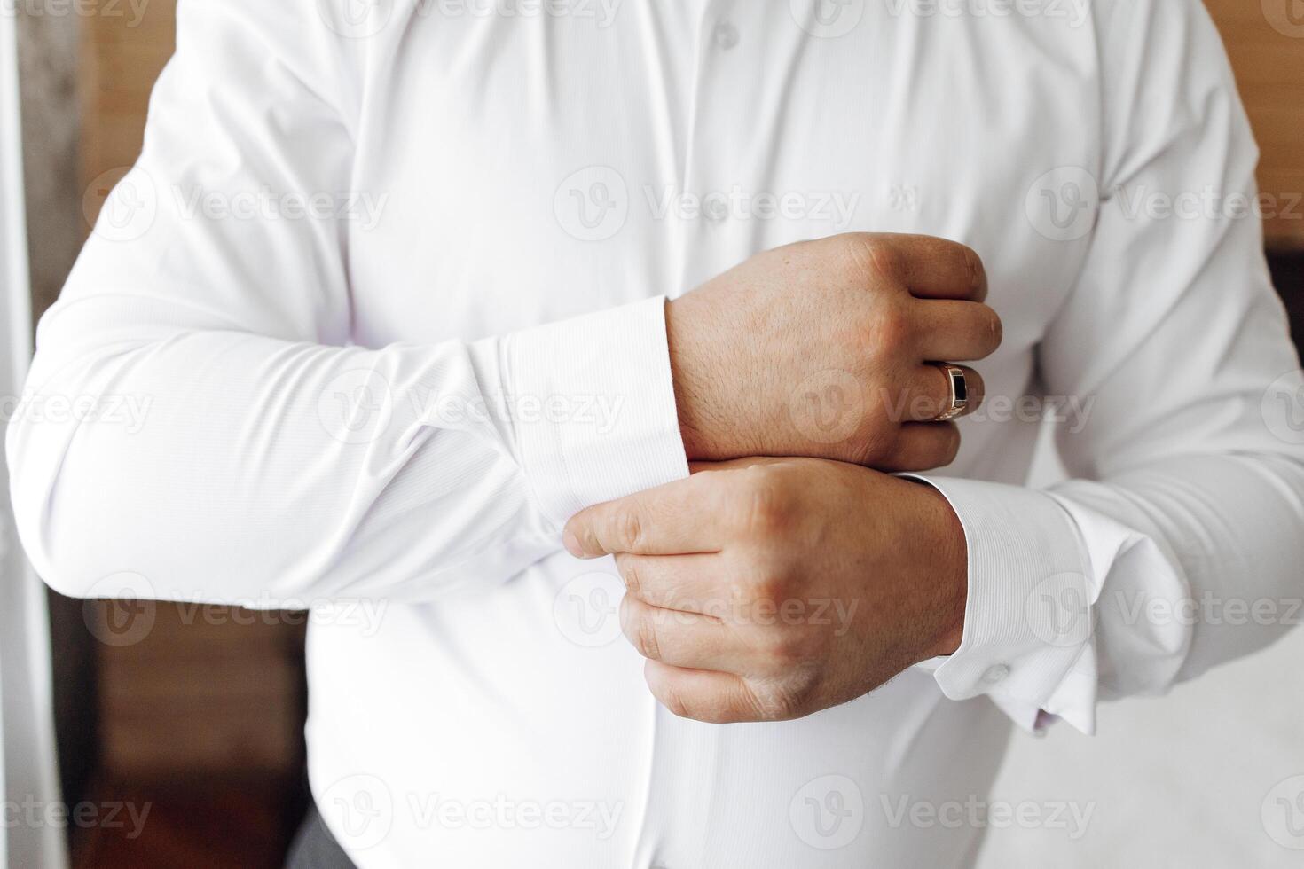 A man in a white shirt is getting ready to put on his wedding ring. He is adjusting his shirt and sleeves, and his hands are visible. Concept of preparation and anticipation for a special occasion photo