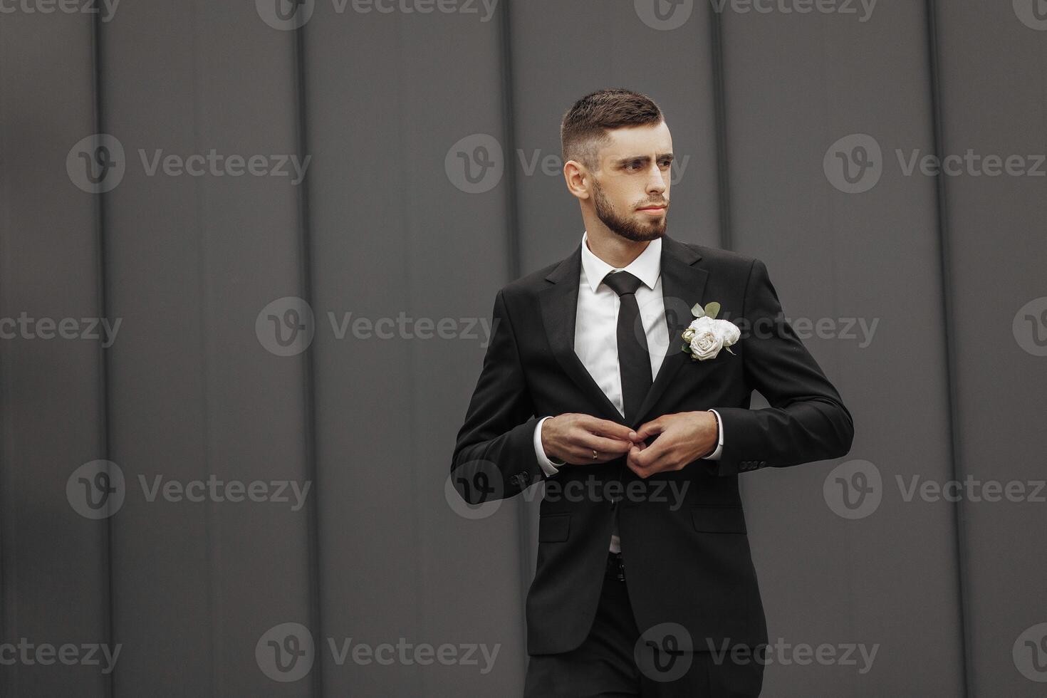 A man in a suit and tie is standing in front of a wall. He is adjusting his tie and holding a flower in his hand. Concept of formality and elegance, as the man is dressed in a suit photo