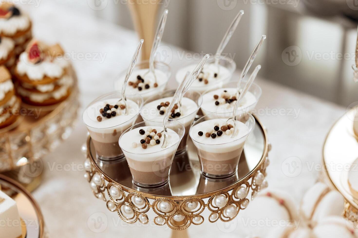 A dessert table with a variety of desserts, including cupcakes and a dessert with a spoon. The desserts are served in clear plastic cups and are arranged on a gold tray photo