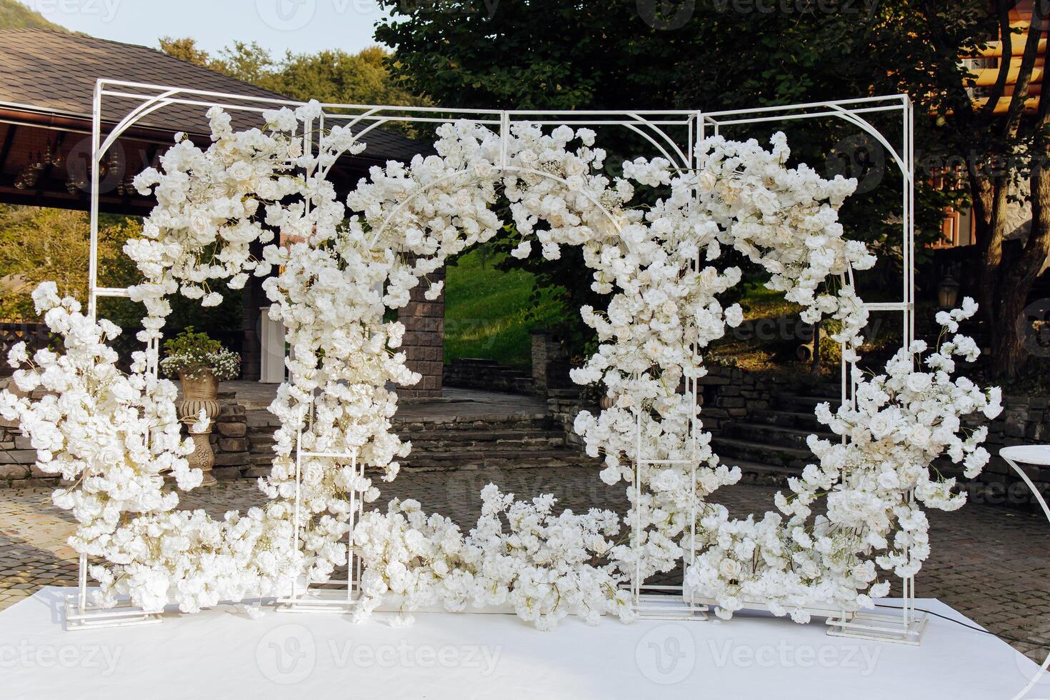 A white archway with flowers is set up in a garden. The archway is made of metal and has a white color. The flowers are white and are arranged in a way that they look like they are blooming photo