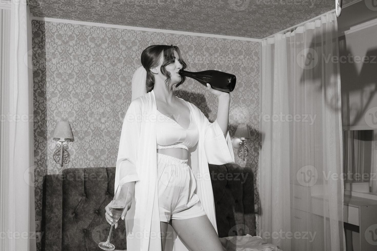 A woman in a white gown is drinking from a bottle of wine photo