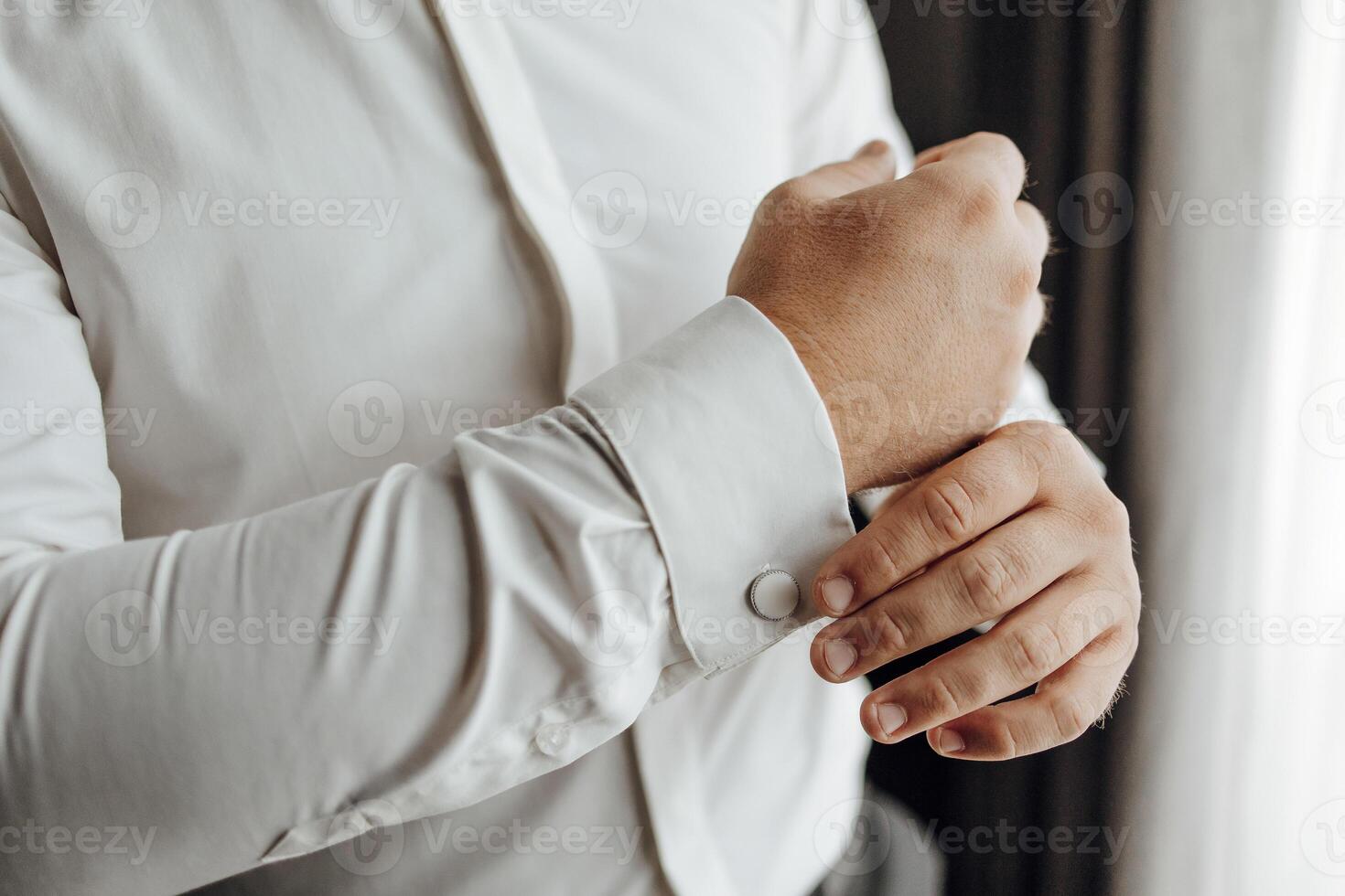A man is getting dressed in a white shirt and is adjusting his cuff. Concept of formality and attention to detail, as the man takes care to properly dress himself photo