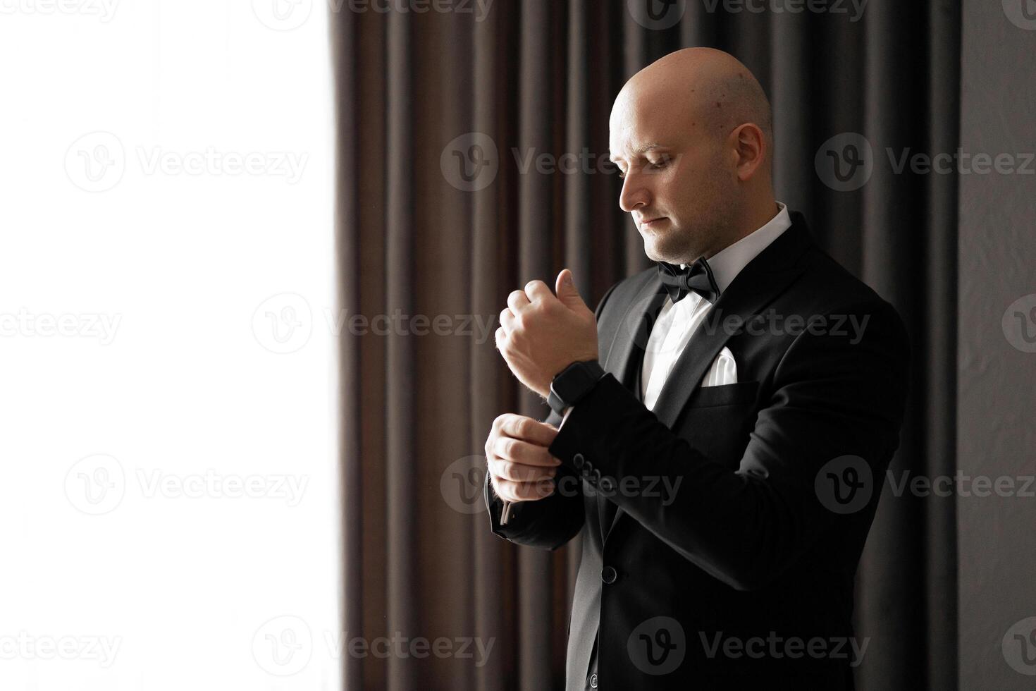 A man in a suit is getting ready to wear a bow tie. He is adjusting it and looking at the camera. Concept of formality and attention to detail photo