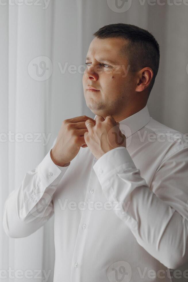 A man is getting ready to dress up in a white shirt. He is adjusting his collar and sleeves photo