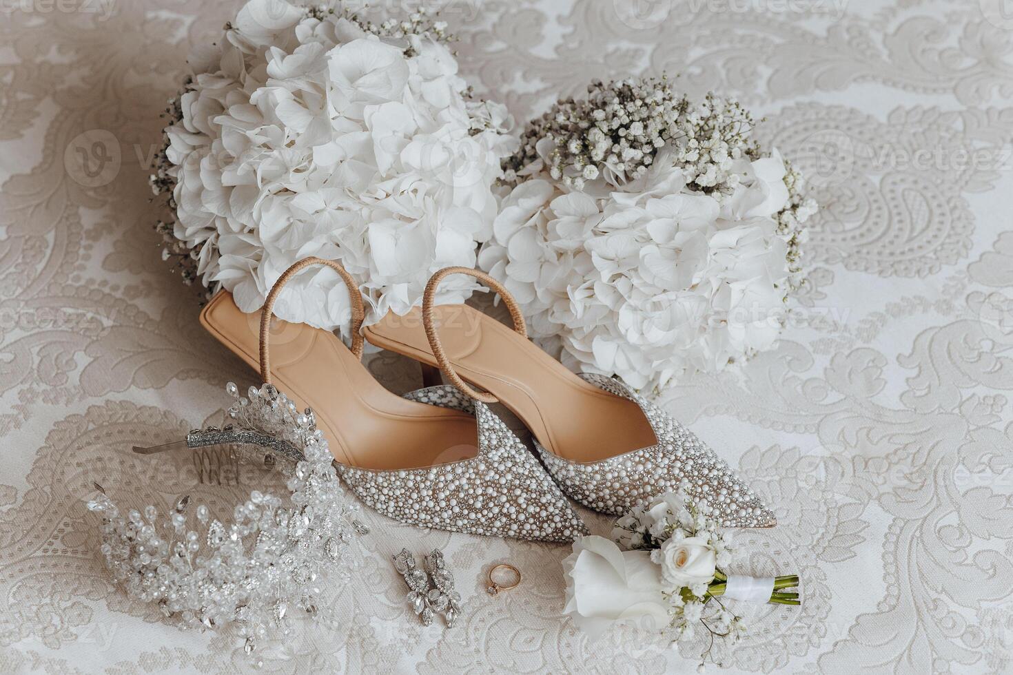 A pair of high heels and a bouquet of white flowers are displayed on a bed. The shoes are adorned with glitter and the flowers are fresh and white. Concept of elegance and sophistication photo
