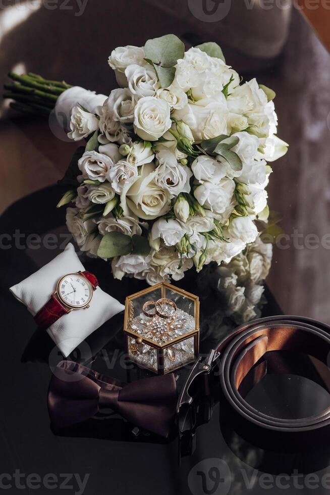 A white bouquet of flowers sits on a table next to a watch and a belt photo