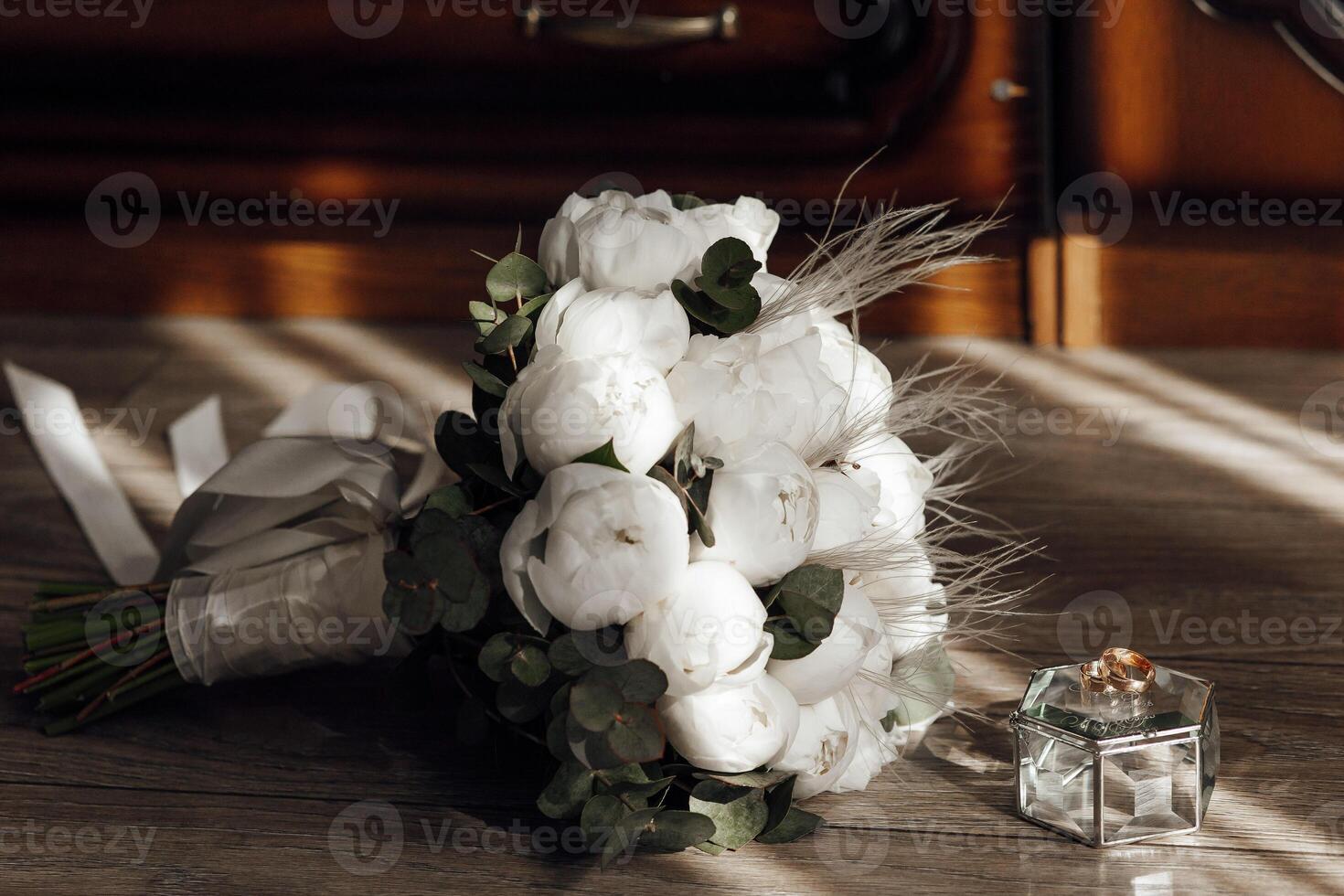 A bouquet of white flowers sits on a wooden table next to a small box. The flowers are arranged in a way that they look like they are about to be arranged in a vase photo