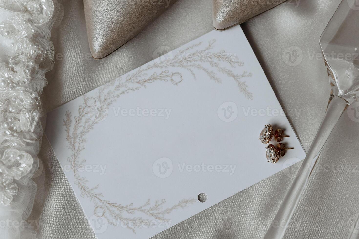 A white card with a wreath design sits on a table with a pair of earrings and a glass photo