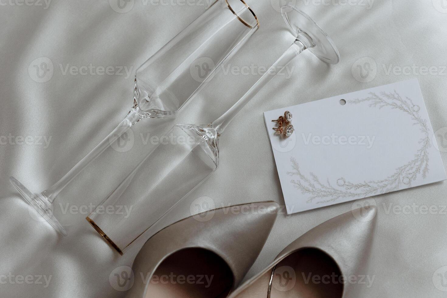 A pair of high heels and two champagne flutes are on a bed. The champagne flutes are gold and the shoes are white photo