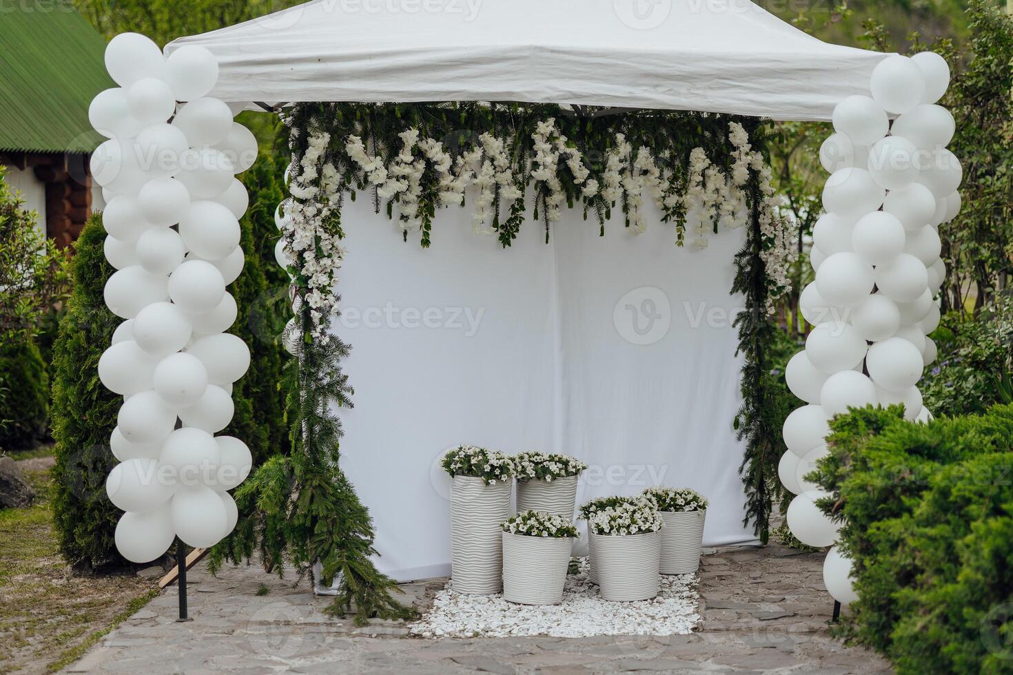 A white tent with white balloons and flowers is set up in a garden. The balloons are arranged in a way that creates a sense of celebration and festivity photo