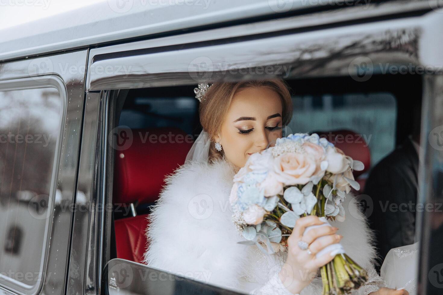 A bride is holding a bouquet of flowers in a car. The car is black and has a red seat. The bride is wearing a white fur coat and a tiara photo