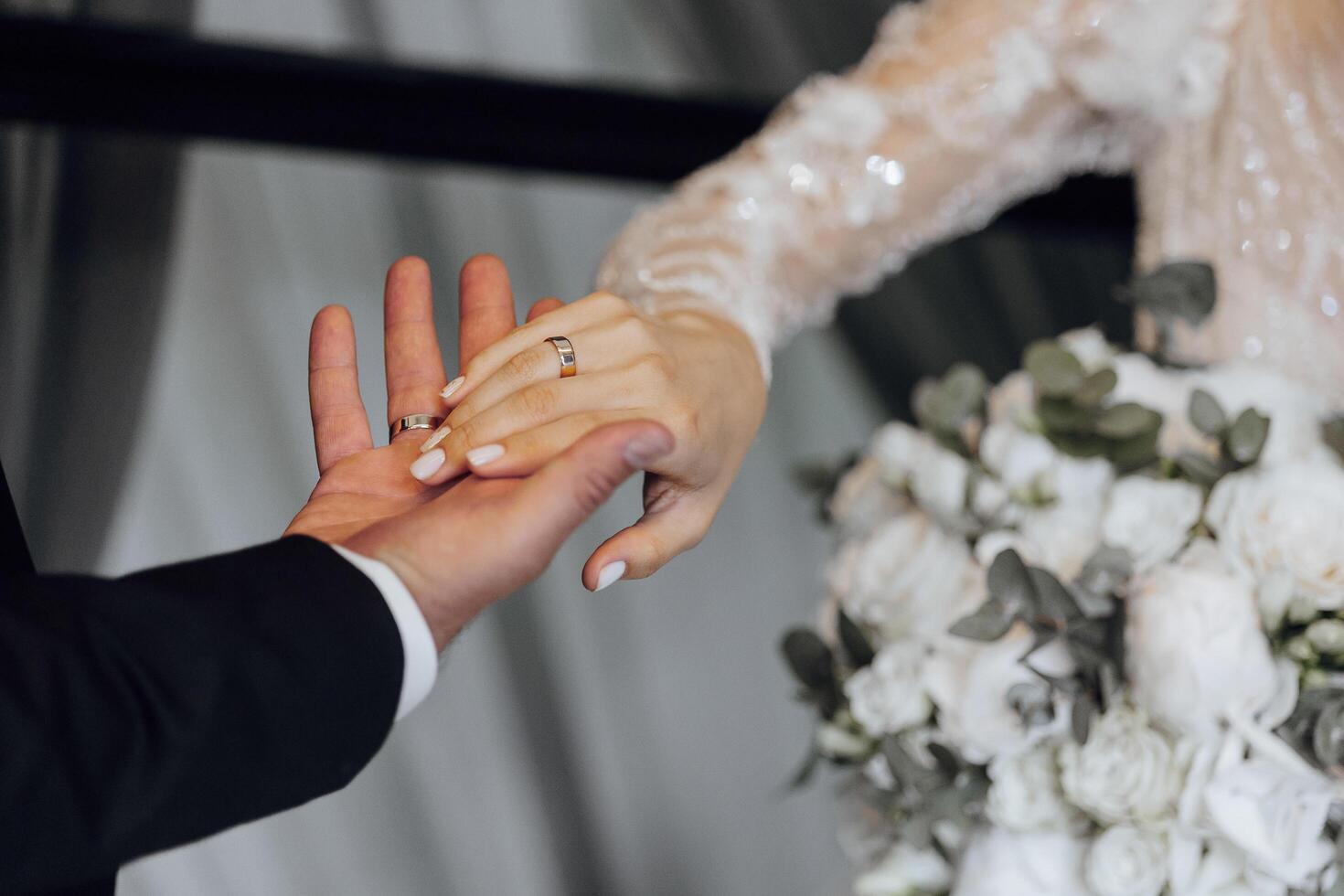 A bride and groom are holding hands, with the bride wearing a white dress and the groom wearing a wedding ring photo