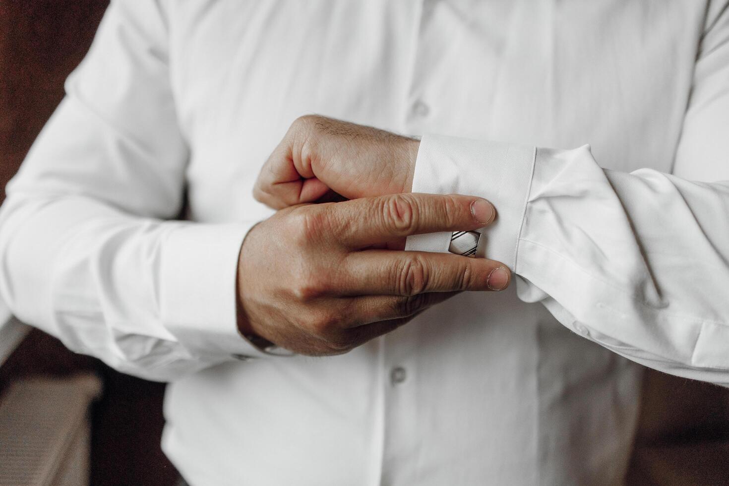 A man is getting dressed in a white shirt and is adjusting his cuff. Concept of formality and attention to detail, as the man takes care to properly dress himself photo