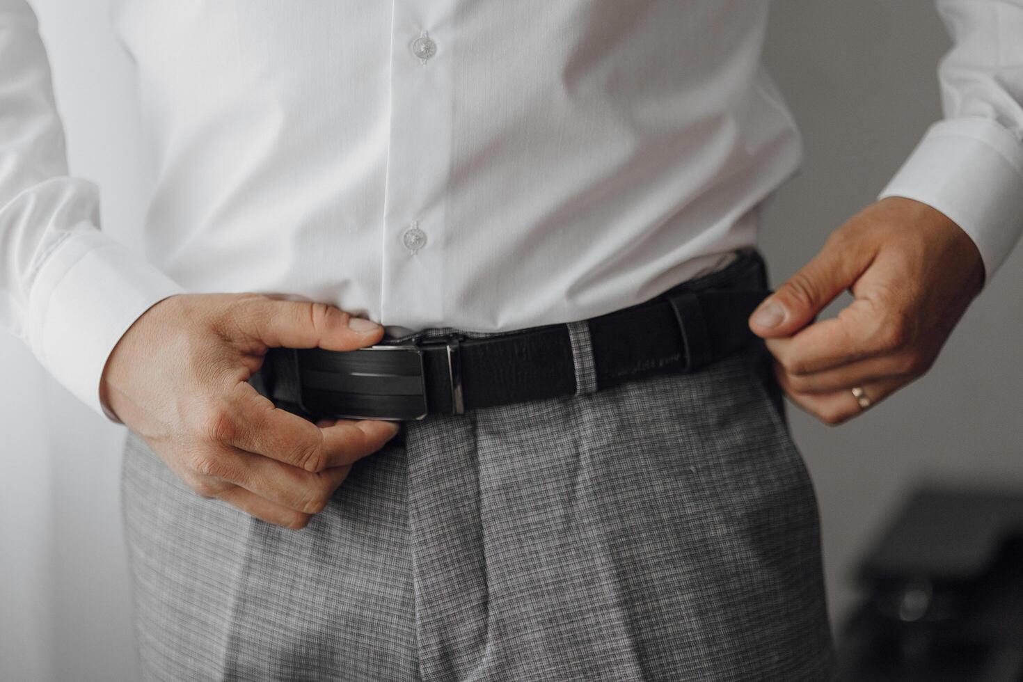 A man is wearing a white shirt and gray pants. He is adjusting his belt. Concept of formality and attention to detail photo