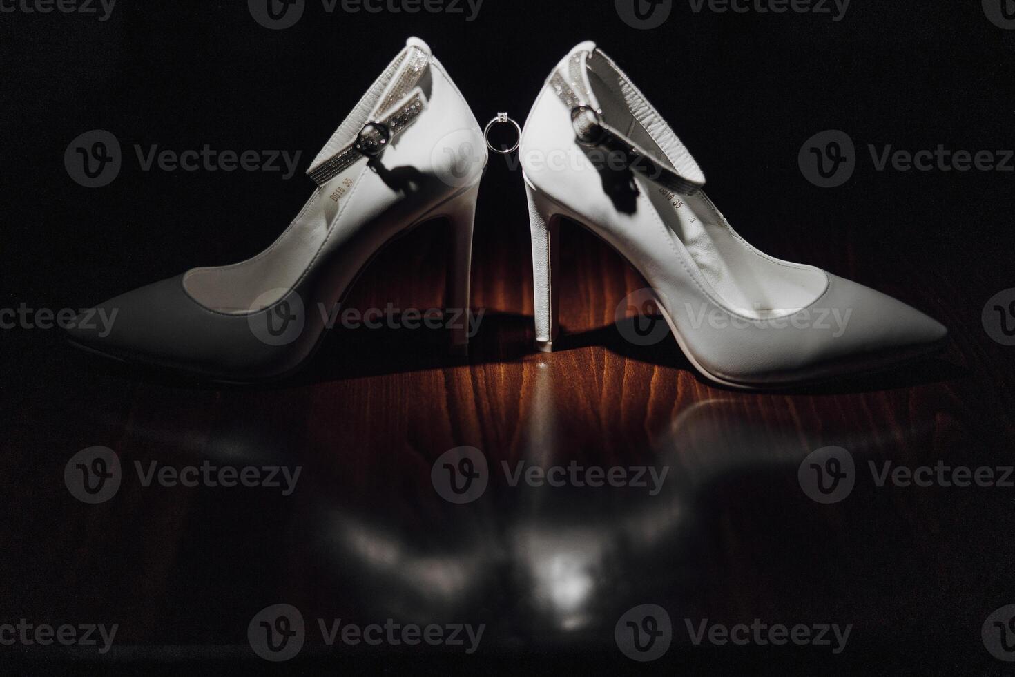 Two white high heels with a silver ring on the front. The shoes are on a wooden table photo