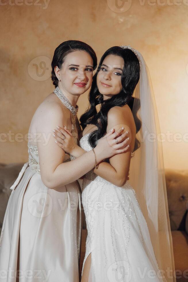 Two women are hugging each other, one of them is wearing a wedding dress. Scene is warm and affectionate photo