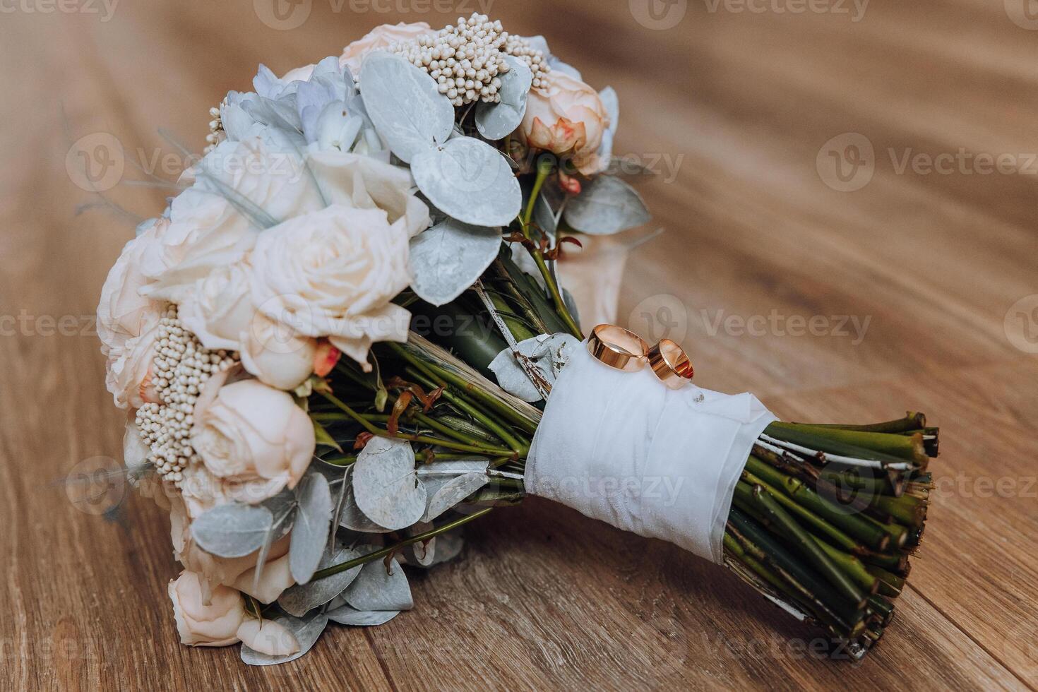 A bouquet of flowers with a white ribbon tied around it. The flowers are white and pink, and there are a few roses in the bouquet. The bouquet is placed on a wooden surface photo