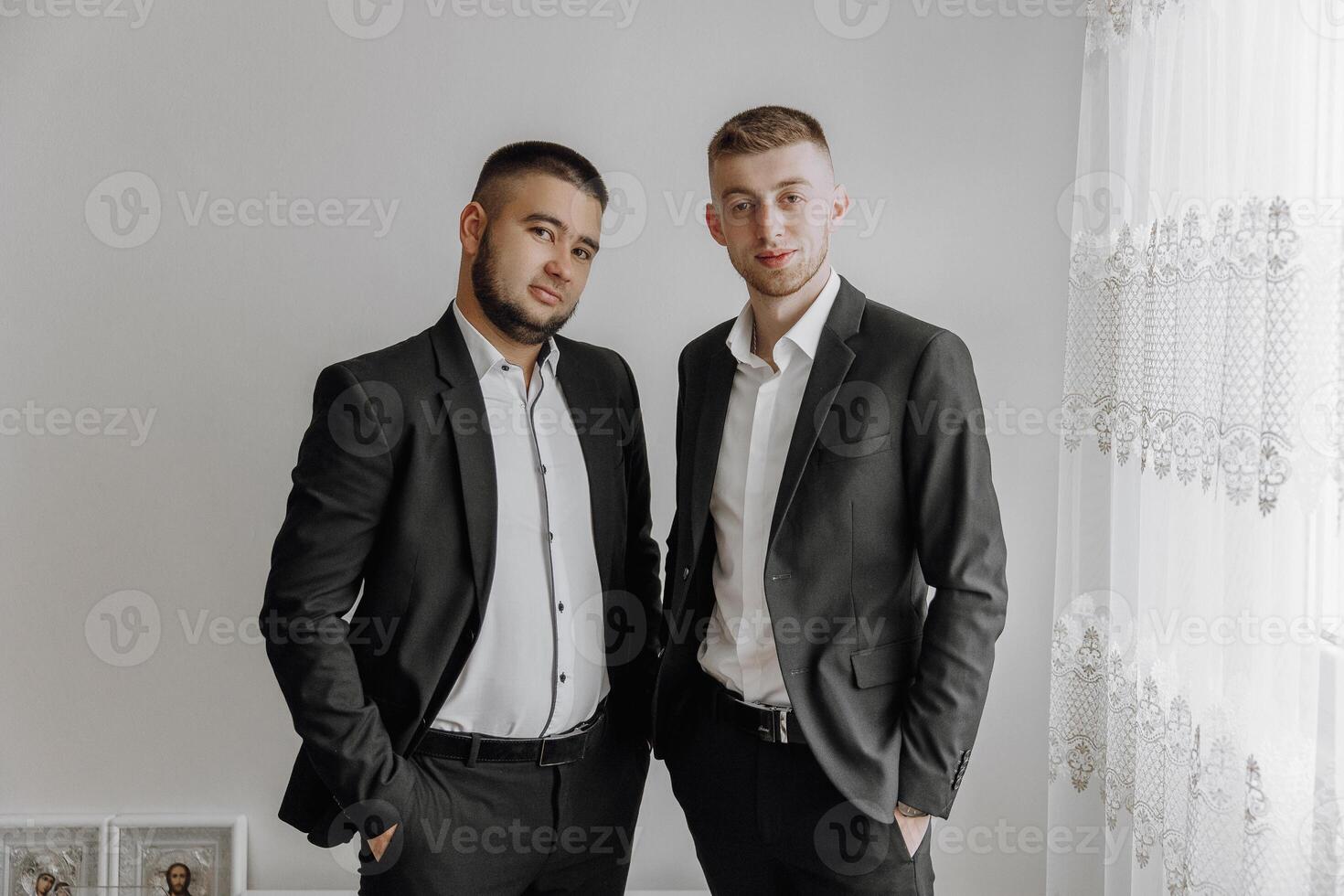 Two men in suits are standing next to each other. They are both wearing white shirts and black suits photo