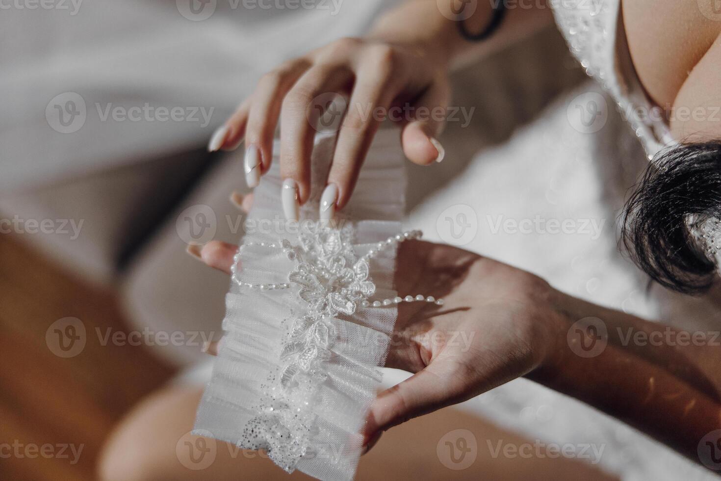 A woman is holding a white lace train with a pearl and lace design. The train is white and has a delicate, elegant appearance photo