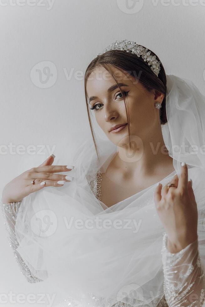 A woman is wearing a white dress and a veil. She is holding her hands up and has a sad expression on her face photo