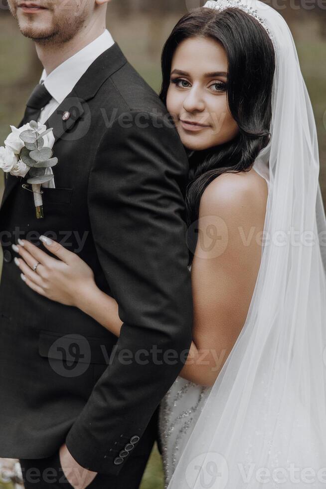 A bride and groom are posing for a picture. The bride is wearing a white dress and the groom is wearing a black suit. They are both smiling and looking at the camera. Concept of happiness and love photo