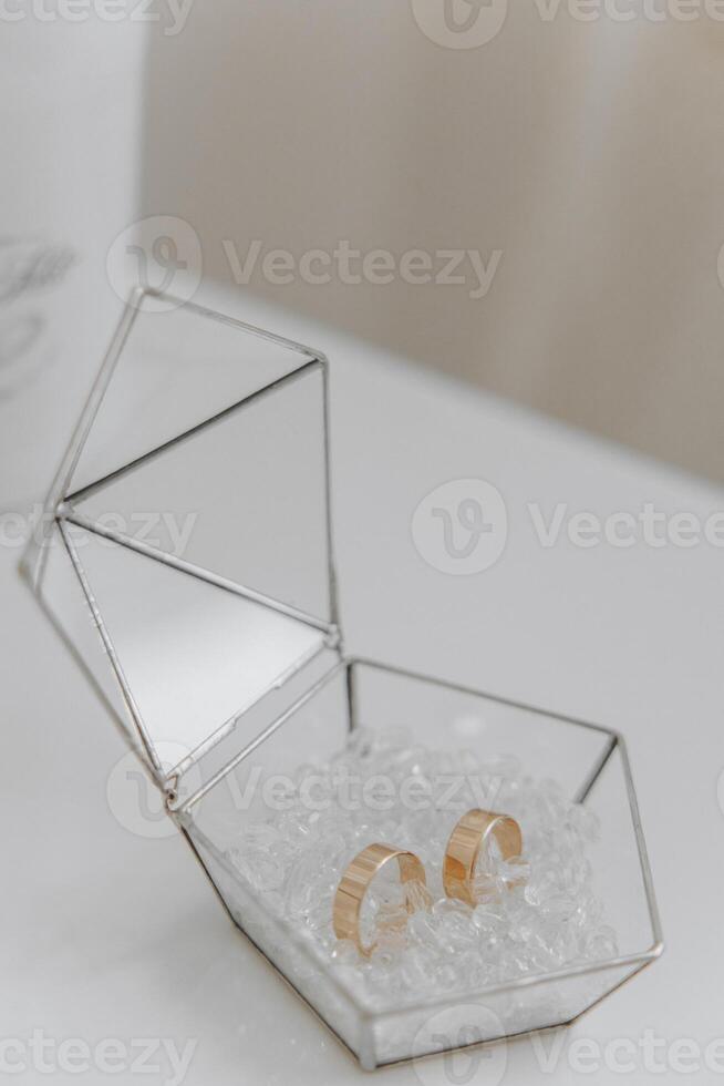 A small box with a pair of gold earrings inside. The box is made of glass and has a triangular shape. The earrings are placed on top of a bed of white beads photo