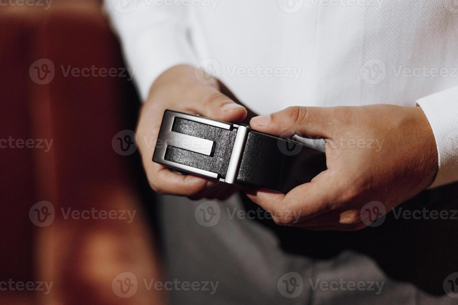 A man is holding a belt in his hand. The belt is black and has a silver buckle photo