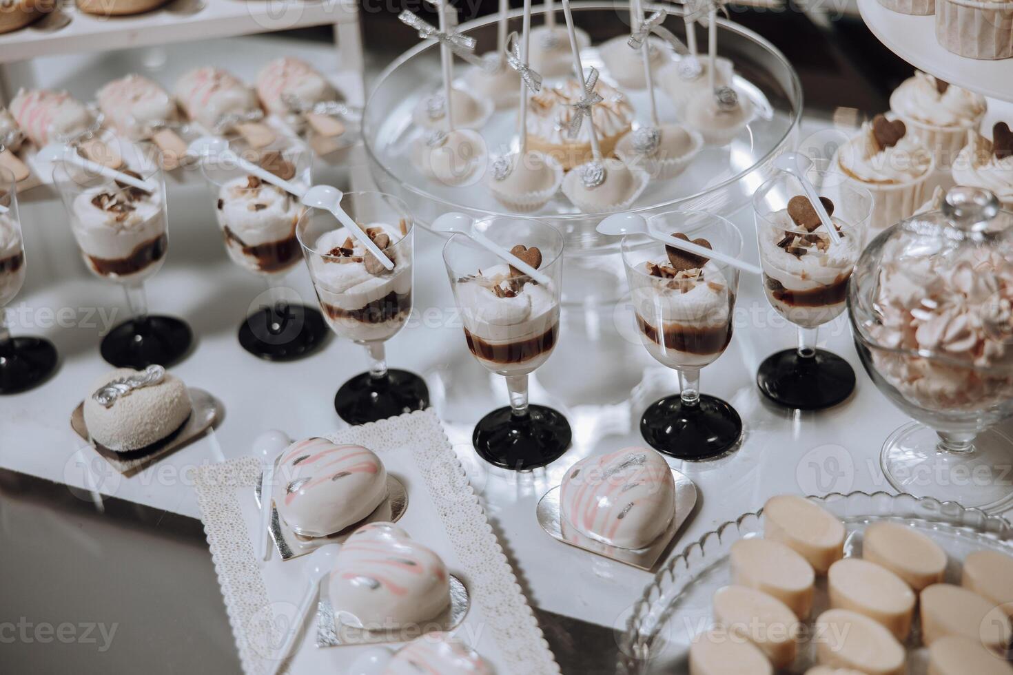 A table full of desserts and drinks, including cupcakes, cakes, and pastries. The table is set up for a party or gathering, and the desserts are arranged in various glassware, such as cups and bowls photo