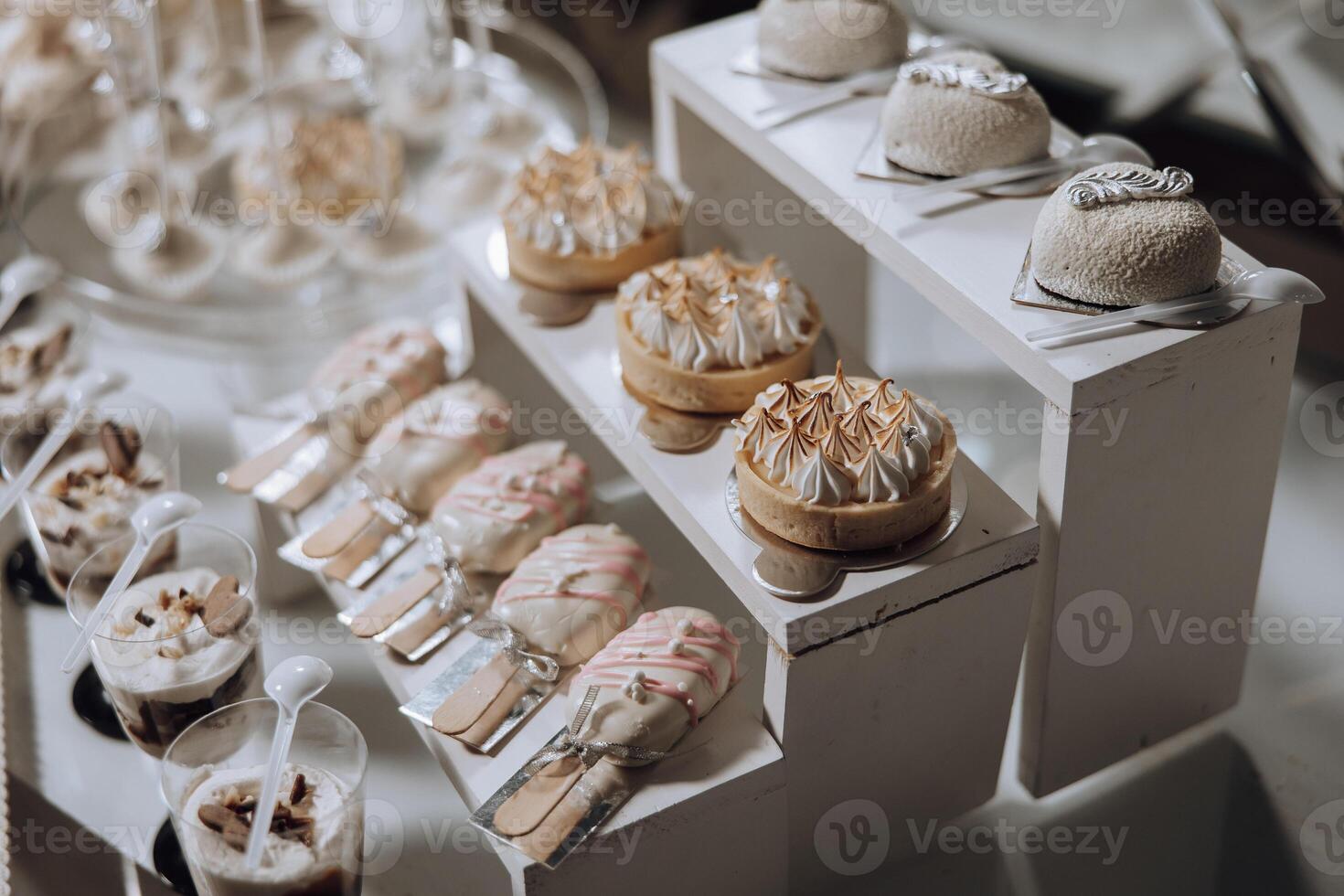 A table full of desserts including cakes, tarts, and other sweet treats. The desserts are arranged on a white table and are presented in small cups. The table is decorated with a variety of desserts photo