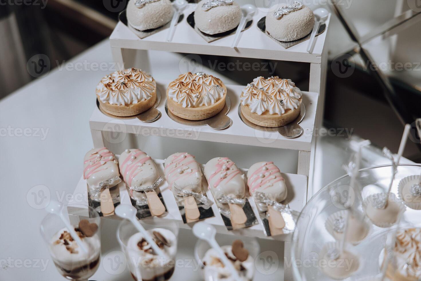A dessert table with a variety of desserts including cupcakes, cookies, and ice cream. The desserts are arranged on a white table and are presented in clear plastic cups photo