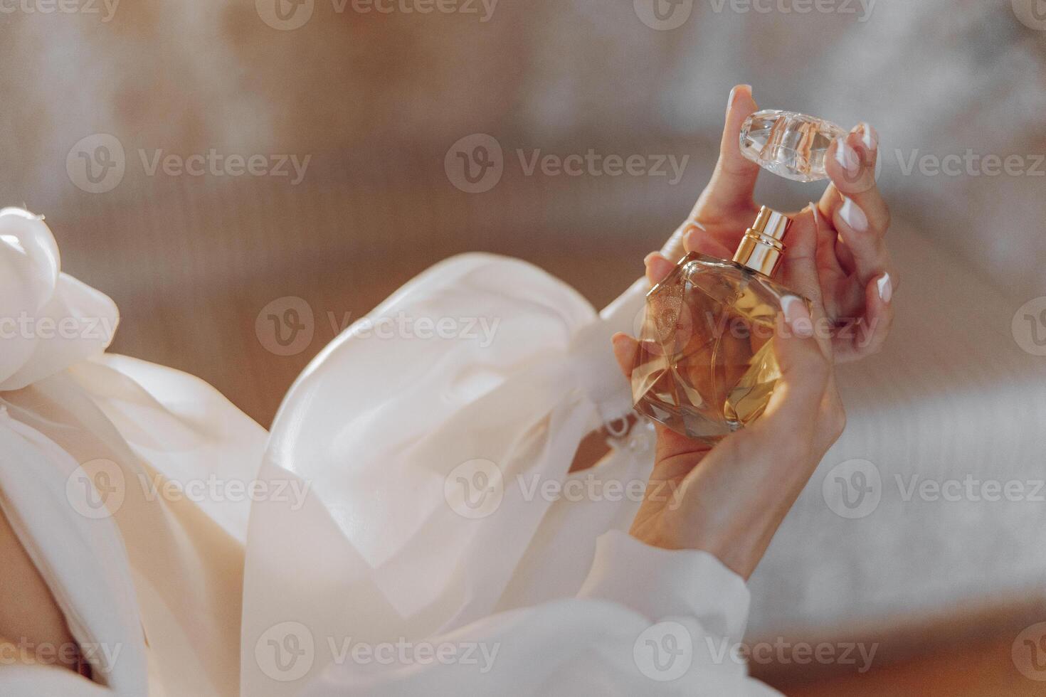 A woman is holding a bottle of perfume. The bottle is made of glass and has a gold cap. The woman is wearing a white blouse and is holding the bottle in her hand photo