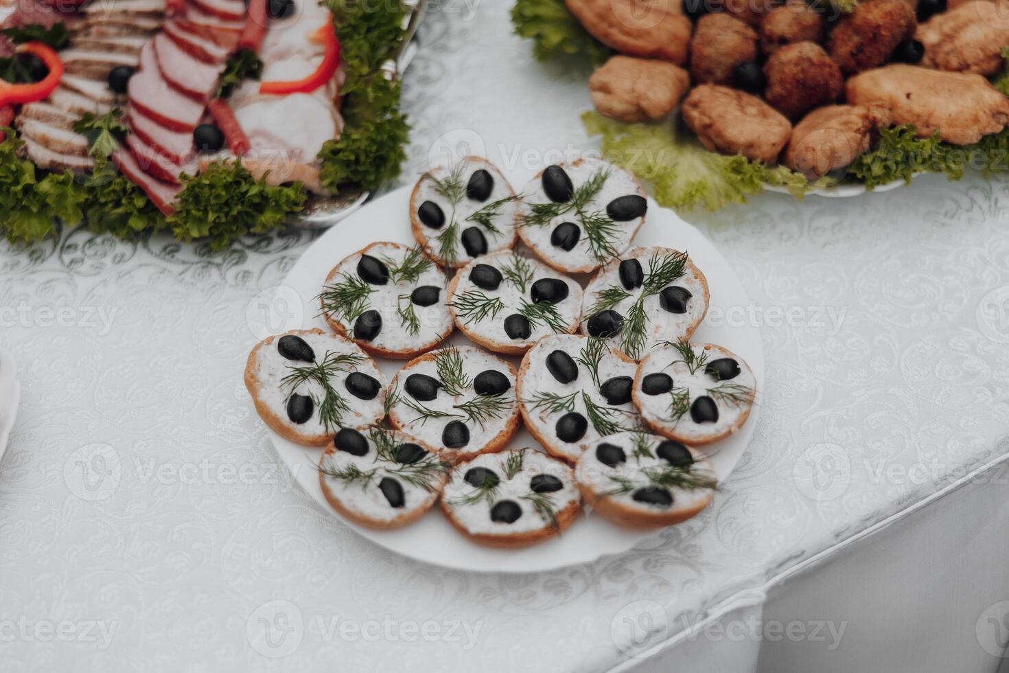 A white plate with a variety of food items including olives, bread, and vegetables. The plate is placed on a table with other plates of food photo