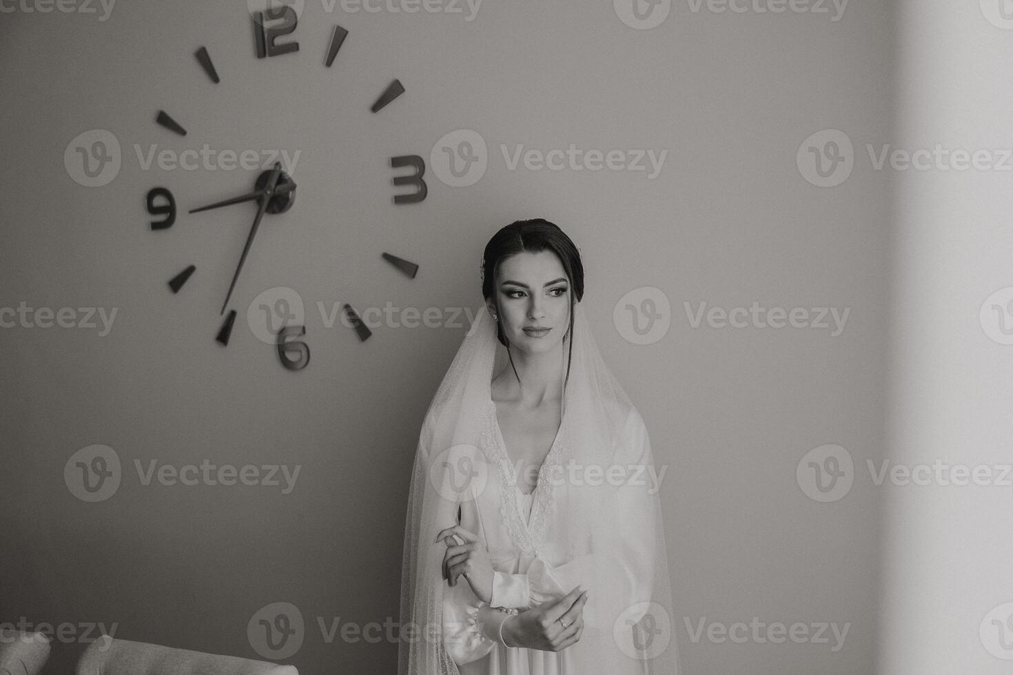 A woman in a wedding dress stands in front of a clock with the hands on the numbers 9 and 3 photo