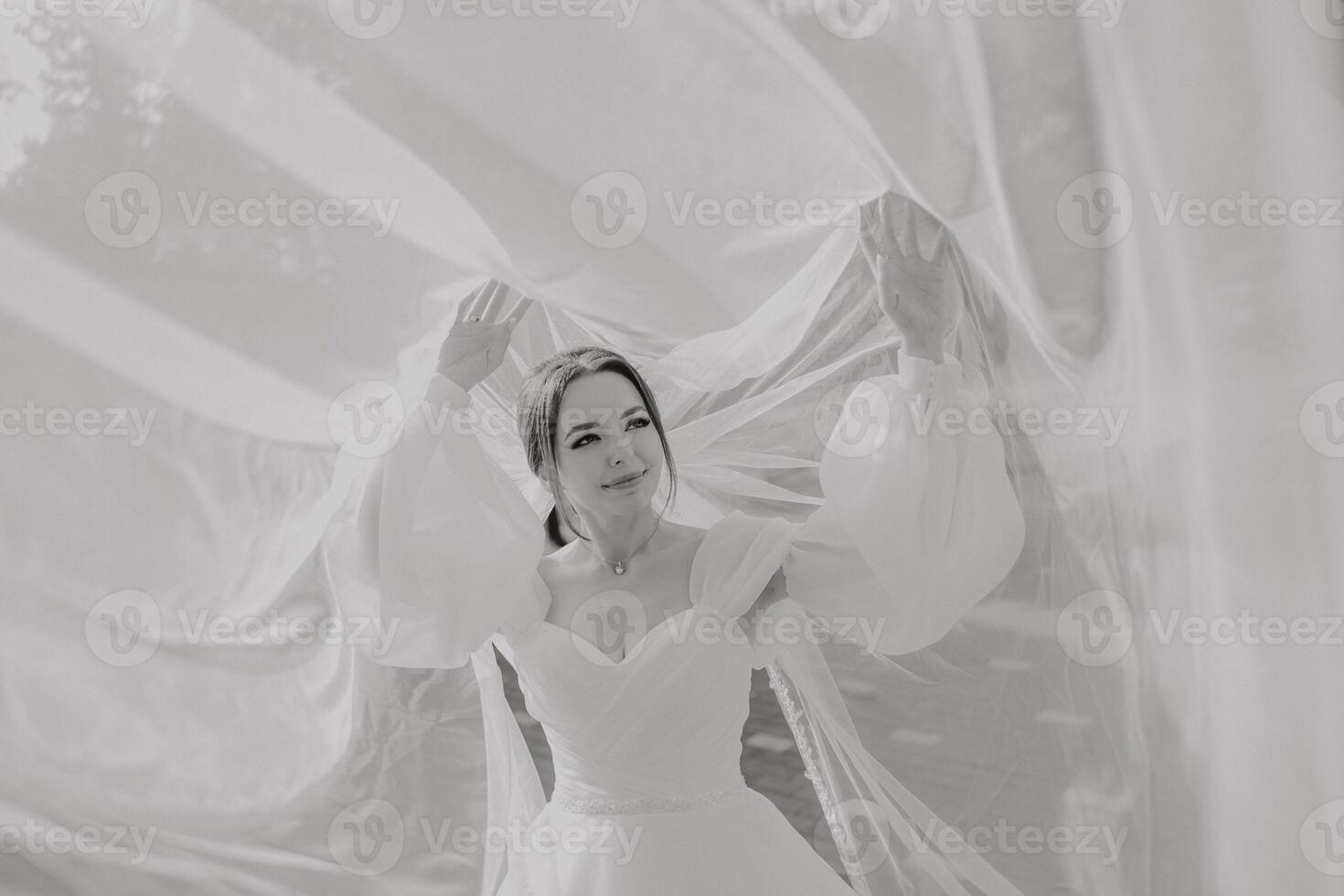 A woman in a white dress is standing in front of a white sheet, with her arms spread out photo