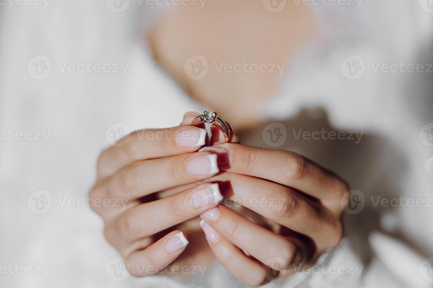 A woman is holding a ring in her hand. The woman is wearing a white dress and has her nails painted. Concept of love and commitment photo