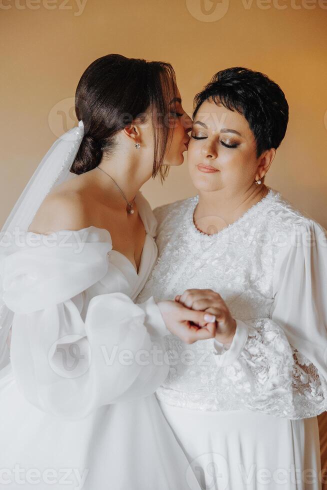 A bride kisses her mother's hand. The bride is wearing a white dress and the mother is wearing a white blouse photo