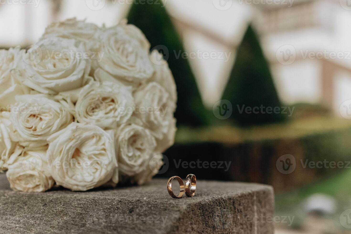 A bouquet of white roses sits on a stone pedestal next to two gold wedding rings. Concept of love and commitment, as the rings symbolize the bond between two people photo