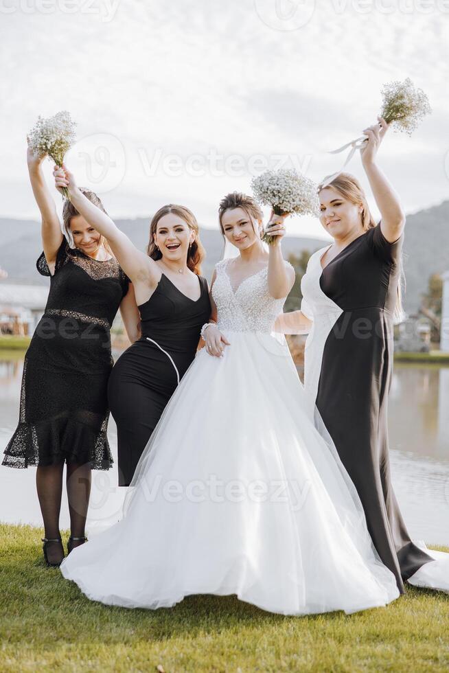 A group of women are posing for a picture, with one of them wearing a white dress. Scene is joyful and celebratory, as the women are smiling and holding flowers photo