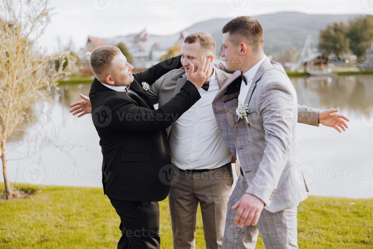 Three men are playing around in a grassy area near a body of water. One of the men is wearing a suit and tie photo