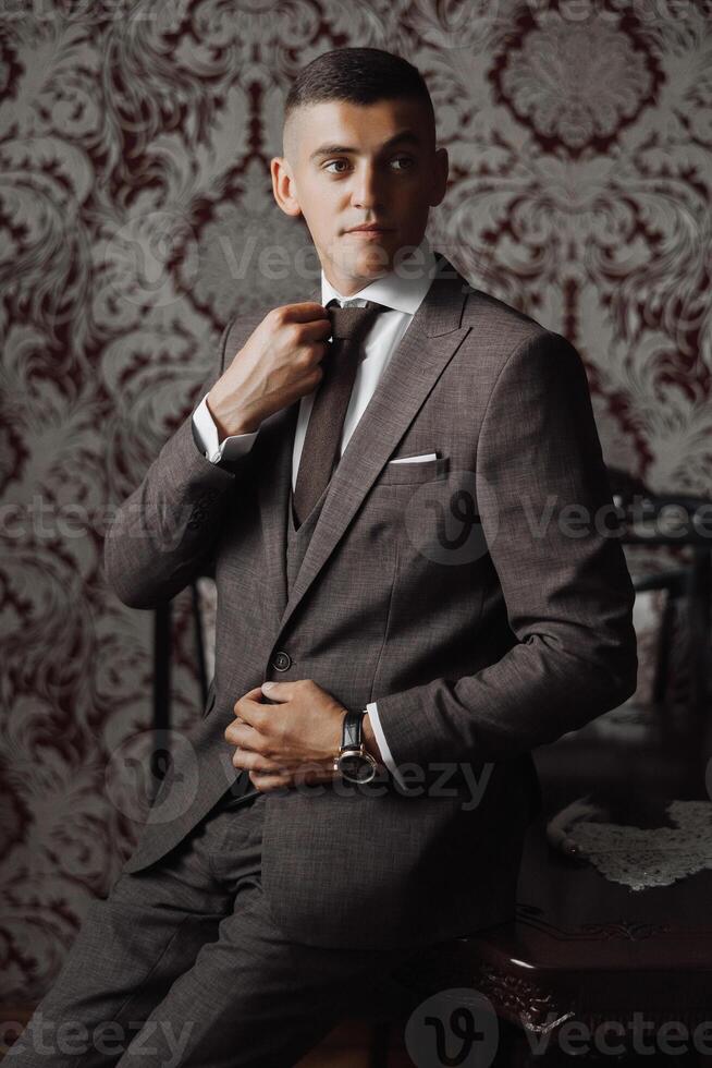 A man in a suit is sitting at a table and adjusting his tie photo