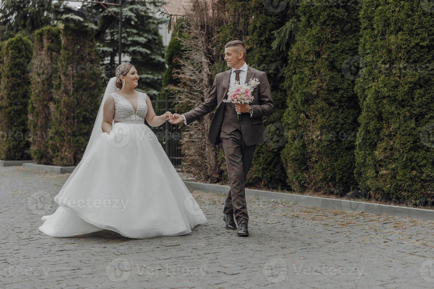 A bride and groom are walking down a street, holding hands photo