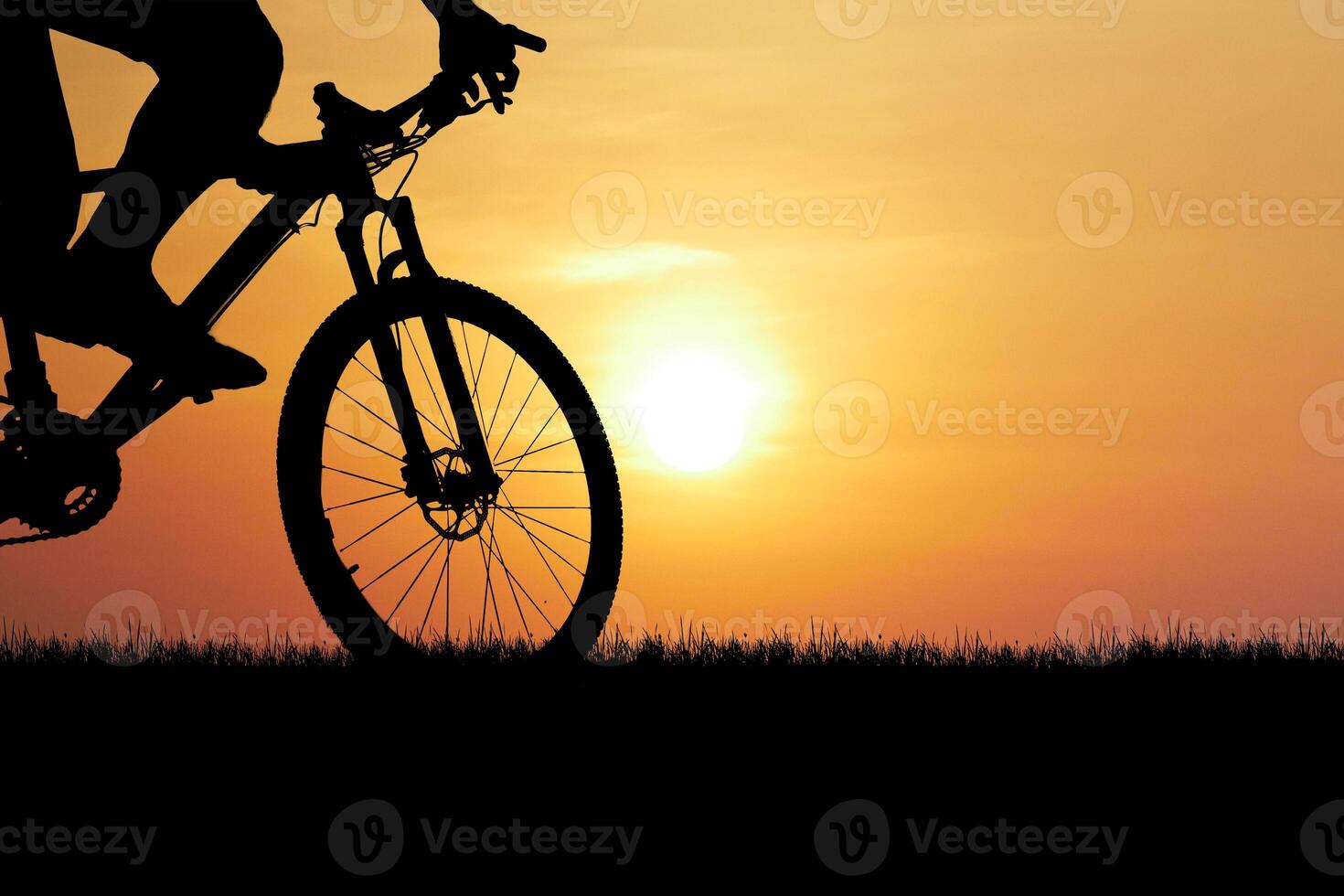 Silhouette of Cyclist Riding Bike at Sunset with Vibrant Orange Sky and Sun in Background photo