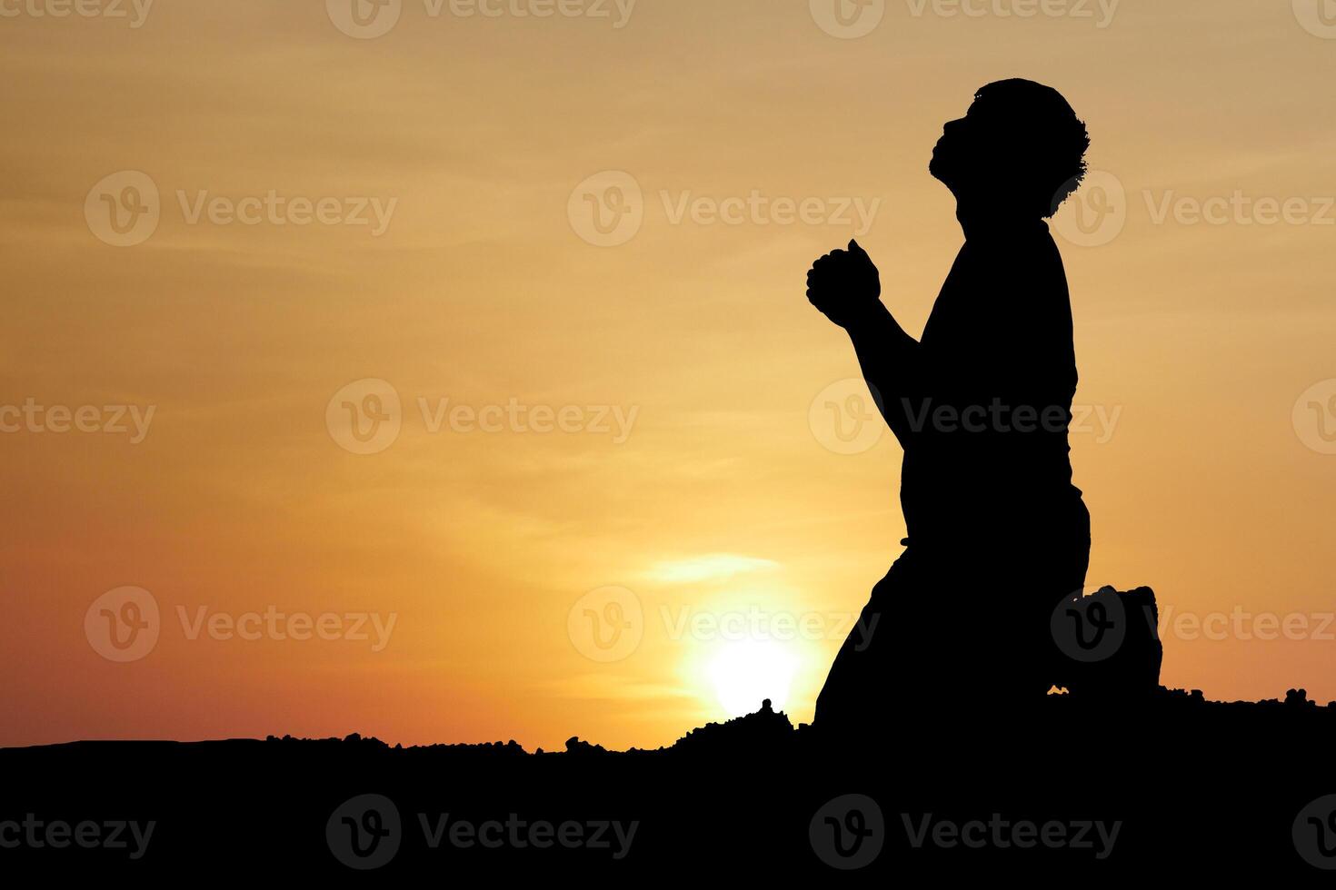 Silhouette of a Person Praying at Sunset with a Beautiful Orange Sky and Sun in the Background photo