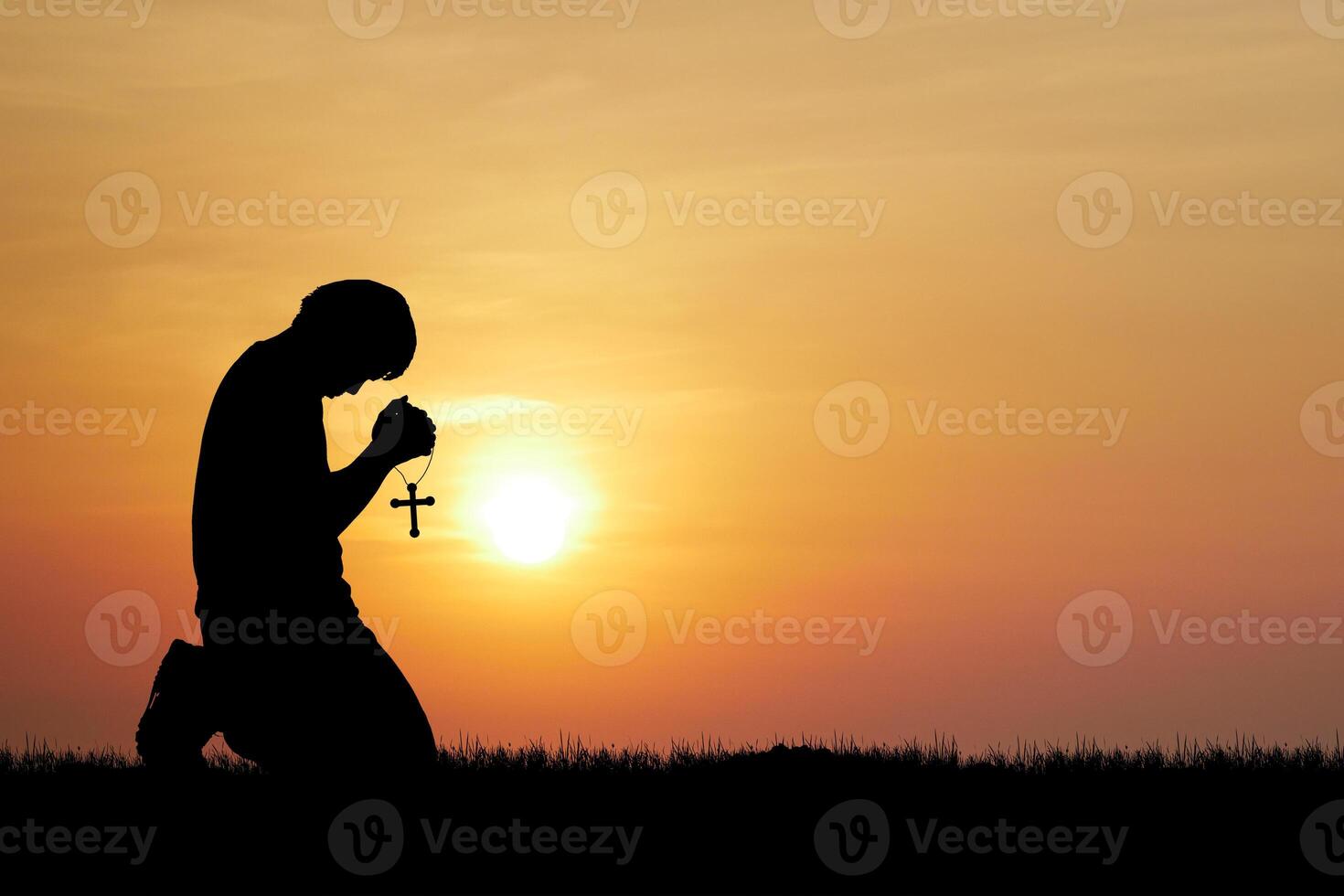 Silhouette of a Person Praying with a Cross at Sunset in a Tranquil Outdoor Setting photo
