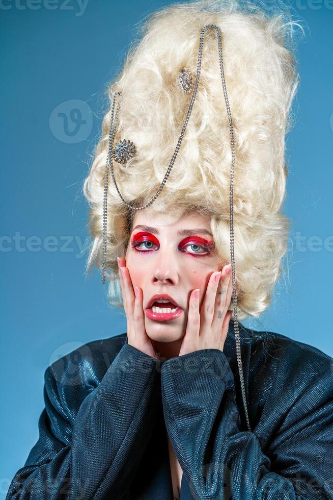 Funny princess with vintage wig and red makeup in blue studio photo